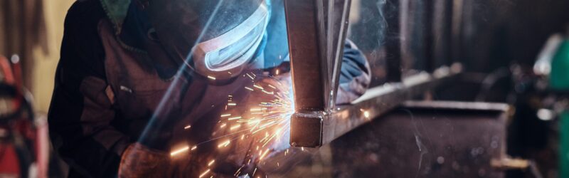 Man is working at metal factory, he is welding a piece of rail using special tools.